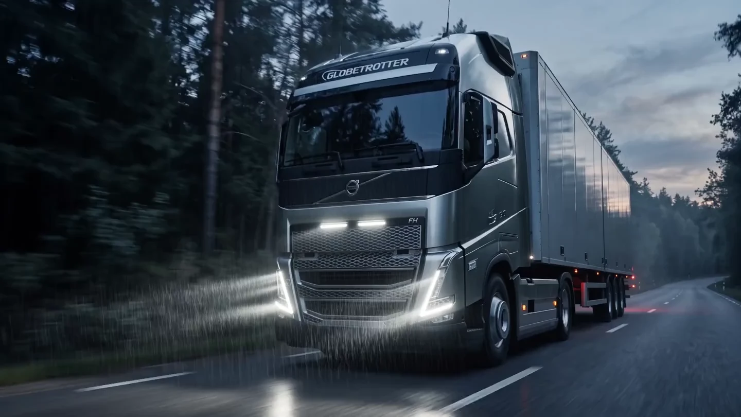 Volvo FH on a wet forest road, approaching its illuminated grille